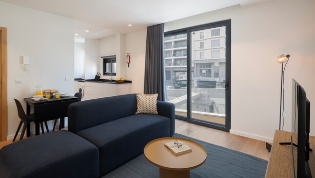 A modern living room with a sofa, a coffee table, and a view of a cityscape through large windows. - Holidays in Funchal - Golden City B (Funchal)