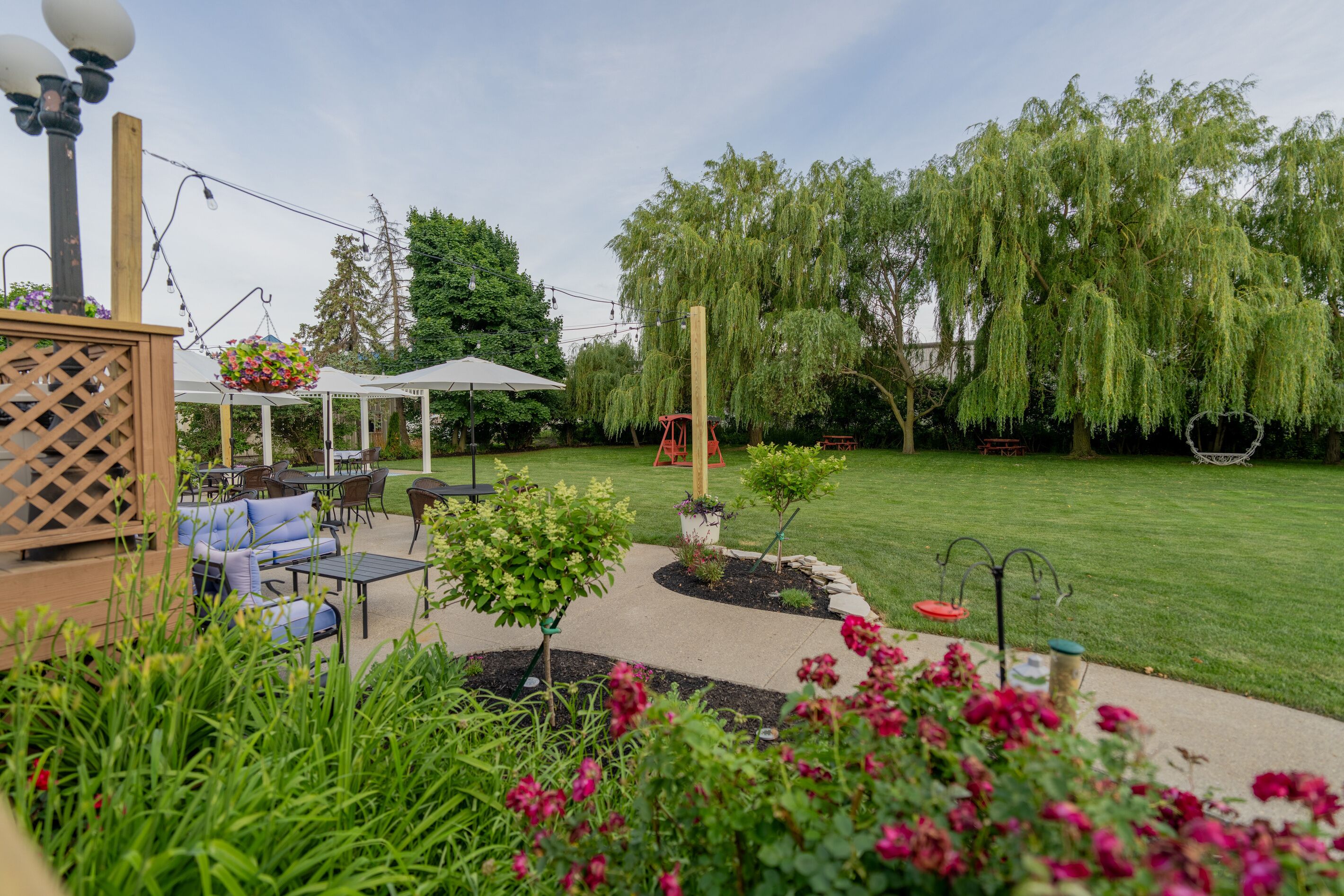 Un espace patio aménagé avec du mobilier d’extérieur, une balançoire et un jardin où poussent différentes espèces de plantes.