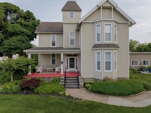 A two-story house with a covered porch, a front door, and a small staircase leading to the entrance. - Stay in Style! Family Getaway by the Erie Shores (Marblehead)