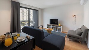 A modern living room with a sofa, a dining table with breakfast items, a TV, and a large window with curtains. - Holidays in Funchal - Golden City C (Funchal)
