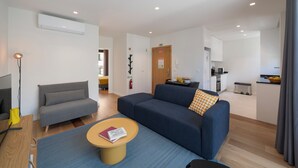A modern living room with a sofa, a coffee table, and a TV. There is a kitchen area in the background. - Holidays in Funchal - Golden City C (Funchal)