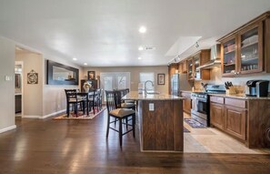 A spacious kitchen with wooden cabinets, a central island, and a dining area with chairs and a table. - Family & Dog Friendly Home in the Heart of Dallas (Farmers Branch)