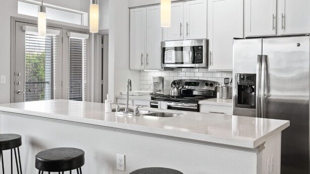 Une cuisine moderne avec des armoires blanches, des appareils en acier inoxydable et des luminaires suspendus.