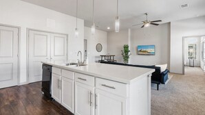 Une cuisine moderne avec des meubles blancs, un grand îlot central, des luminaires suspendus et un ventilateur de plafond.