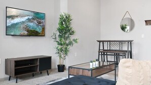 A modern living room with a flat-screen TV, a potted plant, a round mirror, a wooden coffee table, and a sofa. - LUX 2B2B Apt Near Heart of Austin w/Pool & Parking (Austin)