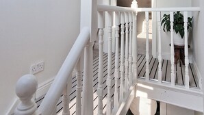 Un escalier avec des balustrades blanches et une main courante, menant à un palier doté d’une lucarne et offrant une vue sur le ciel.