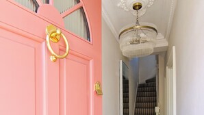 Un couloir avec une porte rose, un lustre et un sol à motifs.