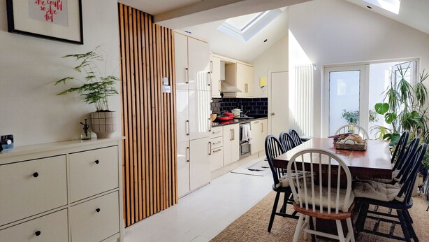 Une cuisine moderne avec des meubles blancs, un séparateur en bois et un coin repas comprenant une table et des chaises.