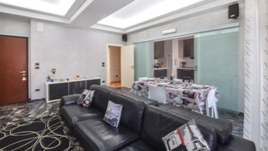 Ein Hotelzimmer mit schwarzem Ledersofa, einem Esstisch für vier Personen und einer kleinen Küche im Hintergrund.