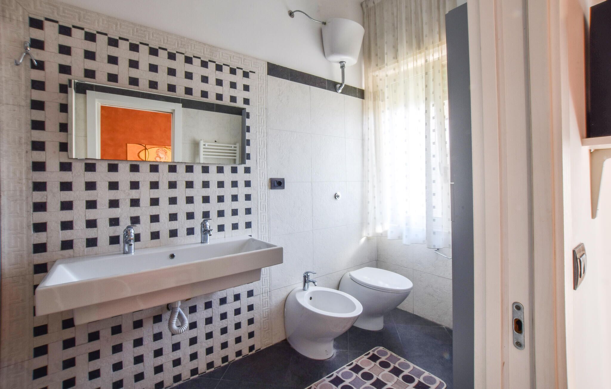 Ein Badezimmer mit kariertem Fliesenrückwand, einem Waschbecken mit Spiegel, zwei Toiletten und einer Duschkabine.
