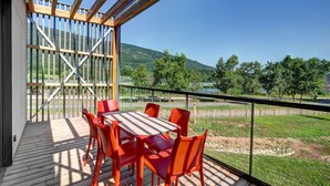 A wooden deck with a table and chairs, overlooking a scenic landscape with trees and hills.
