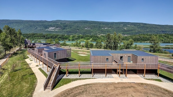 A modern building complex with multiple units, a covered outdoor area, and a scenic view of hills and a lake.