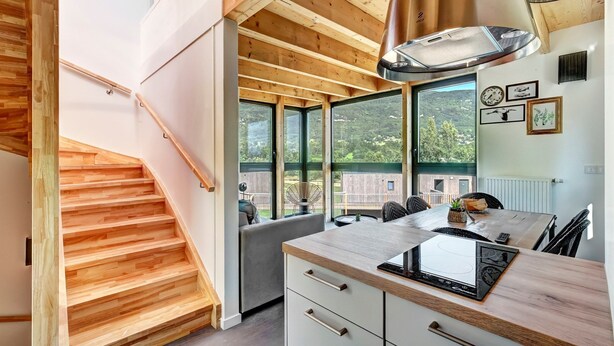 A modern kitchen with wooden beams, large windows, and a view of the outdoors.