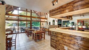 A spacious café with wooden furniture, large windows, and a bar area with coffee machines.