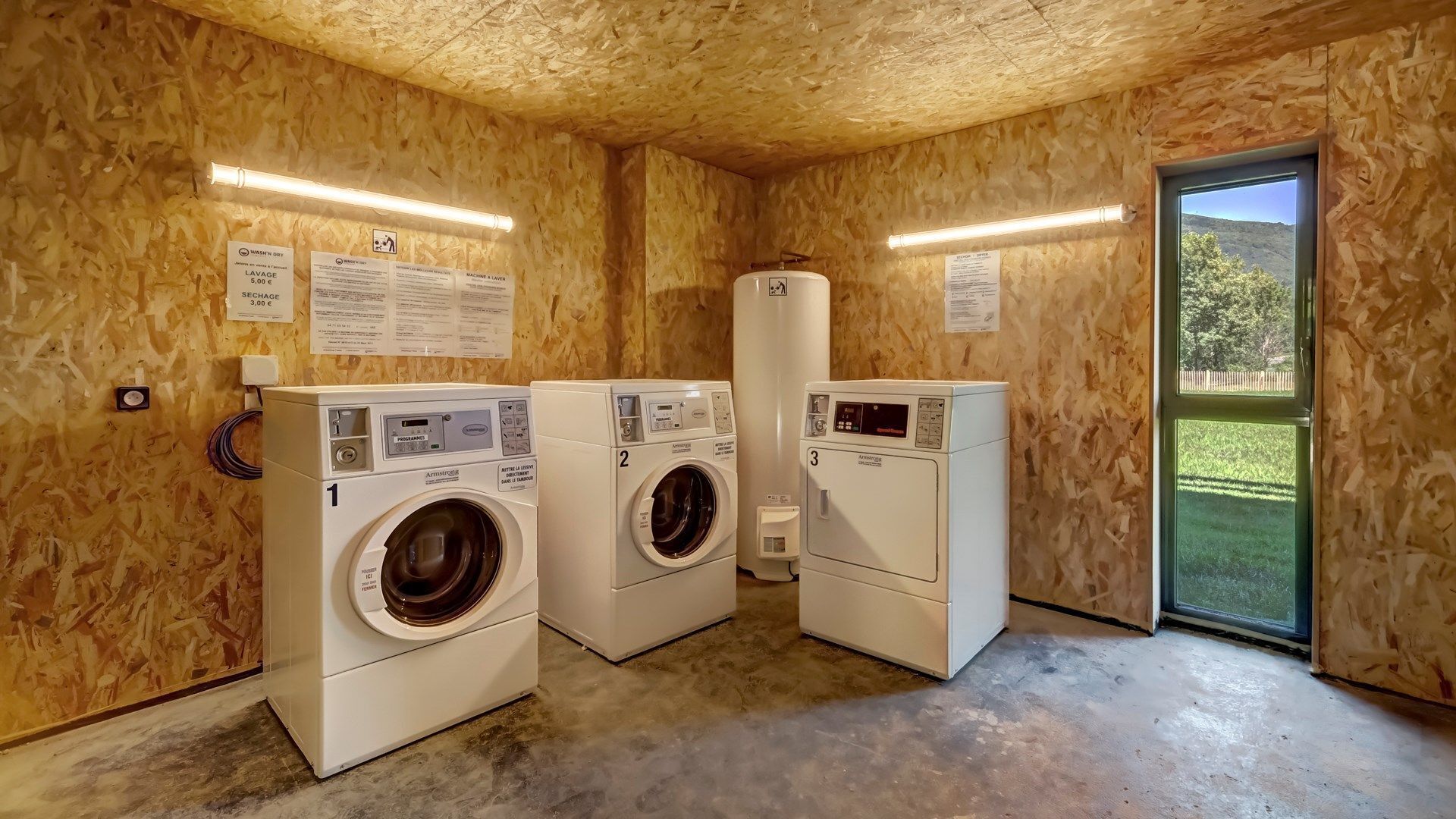 Une buanderie équipée de trois machines à laver, avec des murs en bois et une porte donnant sur l’extérieur.