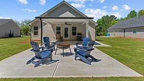 Een huis met een overdekte patio, zitplaatsen buiten en een barbecue.