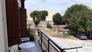 Een balkon met een tafel en stoelen, een witte prullenbak en uitzicht op een parkeerplaats met auto’s en bomen.