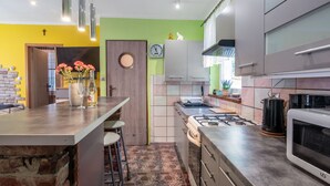Una cocina moderna con estufa a gas, microondas y encimeras de acero inoxidable. Hay un reloj en la pared y un florero con flores en la encimera.