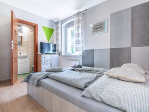 A modern bedroom with a bed, a TV, a window with curtains, and a bathroom visible through an open door. - 2 osobowy by Interhome (Warnowo)