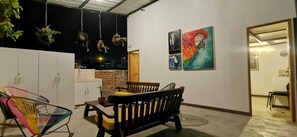 An outdoor seating area with a table and chairs, a hanging plant, and a wall with three paintings.