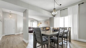 A dining area with a wooden table and chairs, a chandelier, and a view of a living room with a sofa and a lamp. - Magical Villa by Disney  (Kissimmee)