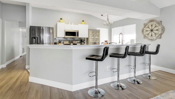 A modern kitchen with a central island, stainless steel appliances, and bar stools. - Magical Villa by Disney  (Kissimmee)
