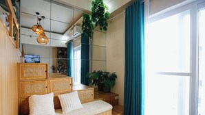 A room with a wooden bench, a mirror, a potted plant, and a large window with curtains. - Experience affordable luxury in our cozy & homey staycation layover pad.  (Lapu-Lapu City)