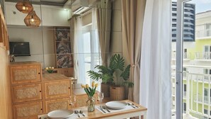 A modern kitchen with wooden cabinets, a dining table set for two, and a large window with curtains. - Experience affordable luxury in our cozy & homey staycation layover pad.  (Lapu-Lapu City)