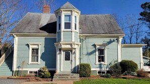 Une maison à deux étages, dotée d’un porche avant imposant, d’une petite structure en forme de tour et d’un chemin en briques menant à l’entrée.