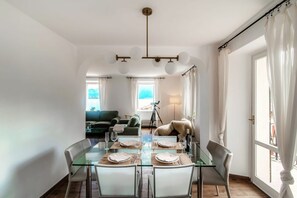 A dining area with a glass table set for four, surrounded by white chairs, a tripod, and a fur throw.