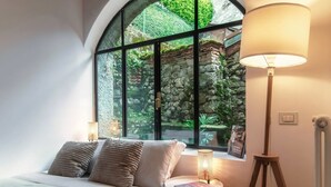 Ein Schlafzimmer mit einem großen Bogenfenster, einem Bett mit Kissen, einer Nachttischlampe und einem kleinen Tisch mit einer Lampe.