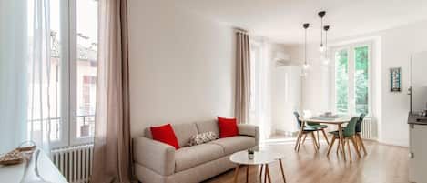 A modern living room with a sofa, dining table, chairs, and a coffee machine.