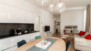 A modern kitchen with white cabinets, a dining table with chairs, and a living area with a sofa and TV. - Dolce - MyHomeinComo (Como)