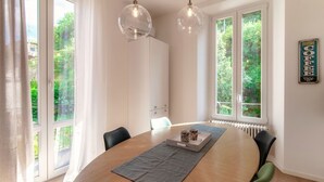 A dining area with a round table, chairs, pendant lights, and a view of greenery through large windows. - Dolce - MyHomeinComo (Como)