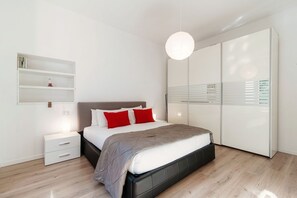A modern bedroom with a bed, bedside tables, a wardrobe, and a hanging light fixture.