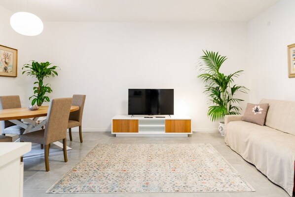 Un salon comprenant un téléviseur, une table à manger, des chaises, un canapé et deux plantes en pot.