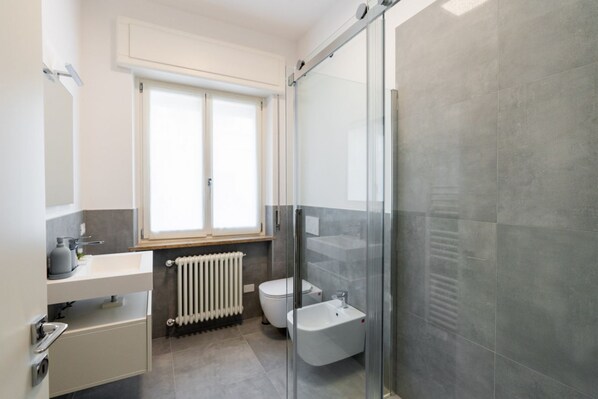 Un baño moderno con cabina de ducha de vidrio, inodoro, bidé y ventana que proporciona luz natural.
