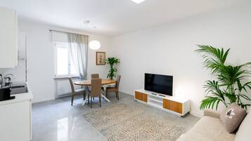 Un soggiorno moderno con TV a schermo piatto, un divano, un'area pranzo con sedie e un angolo cottura con lavello e pensili.