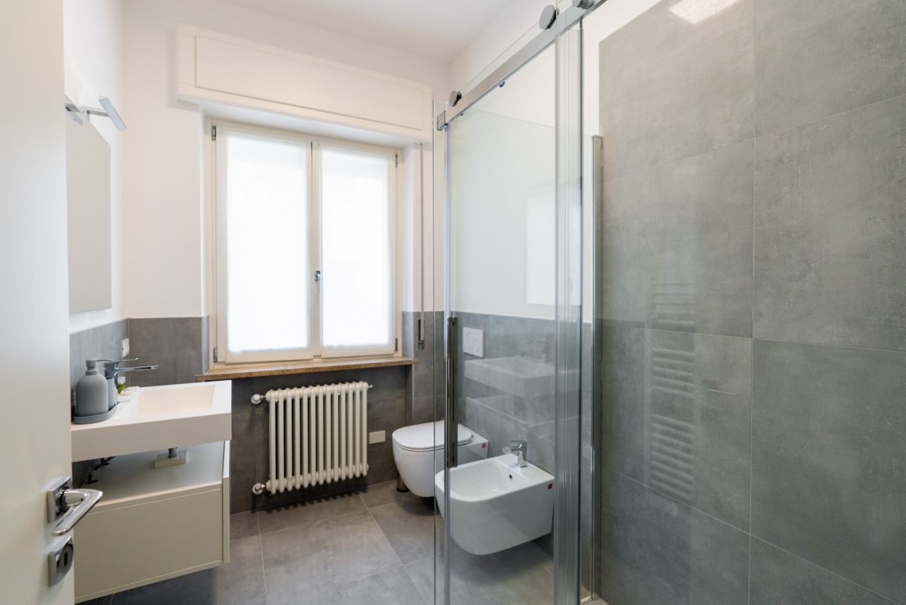 Une salle de bain moderne dotée d’une douche à parois de verre, de toilettes, d’un bidet et d’une fenêtre laissant entrer la lumière naturelle.