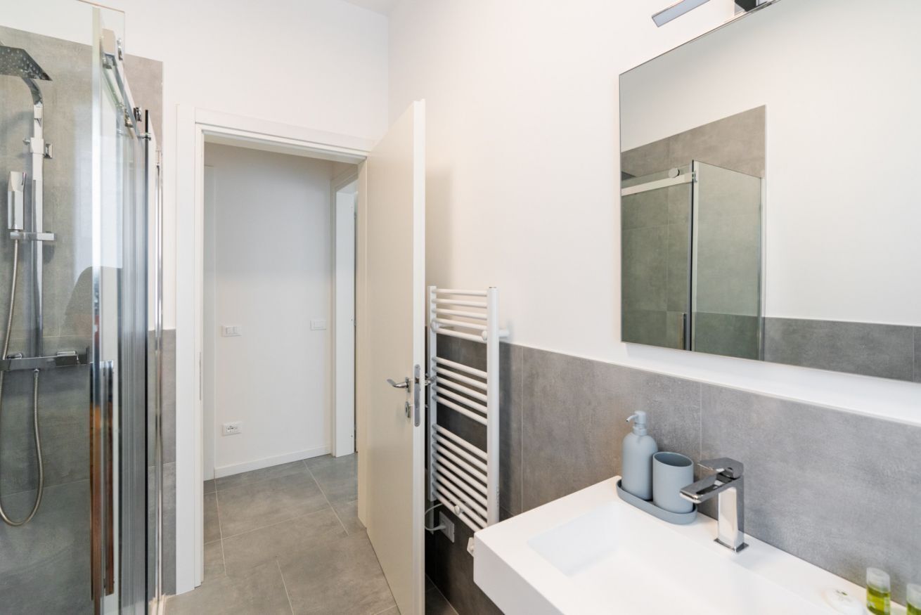 Un baño moderno con cabina de ducha de vidrio, un lavamanos blanco con espejo y un perchero para toallas.