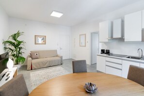 A modern, minimalist living space with a dining area, kitchenette, and a sofa.
