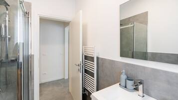 Un bagno moderno con box doccia in vetro, lavandino bianco con specchio sopra e portasciamani.