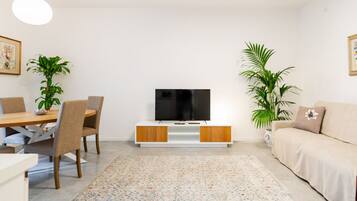 Una sala de estar con televisor, una mesa de comedor, sillas, un sofá y dos plantas en macetas.