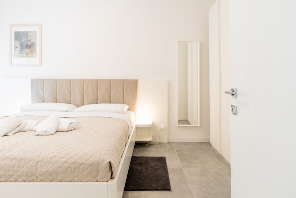 A minimalist bedroom with a bed, bedside table, and a mirror.