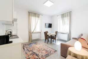 A modern hotel room with a kitchenette, a dining area, a sofa, and a TV.
