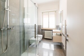 A modern bathroom with a glass shower enclosure, a toilet, a bidet, a sink, and a radiator.