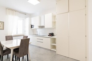 Una cucina moderna con mobili bianchi, un tavolo da pranzo con sedie e una finestra con tende.