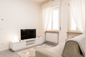 Ein modernes Wohnzimmer mit einem Flachbildfernseher auf einer weißen Unterhaltungsanlage, einem beige farbenen Sofa und einem gemusterten Teppich.