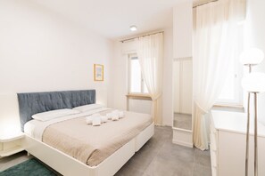 A bedroom with a bed, a bedside table, a window with curtains, a mirror, and a lamp. - Melon Court Residence 3 (Verona)