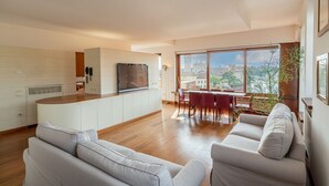 A modern kitchen with a central island, a dining area with a red table and chairs, and a large window offering a city view. - Ponte Pietra Residence (Verona)